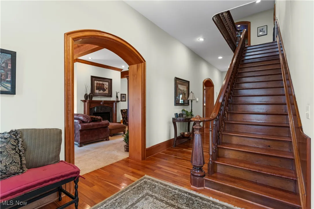 Stairs featuring wood finished floors, a fireplace, baseboards, recessed lighting, and arched walkways