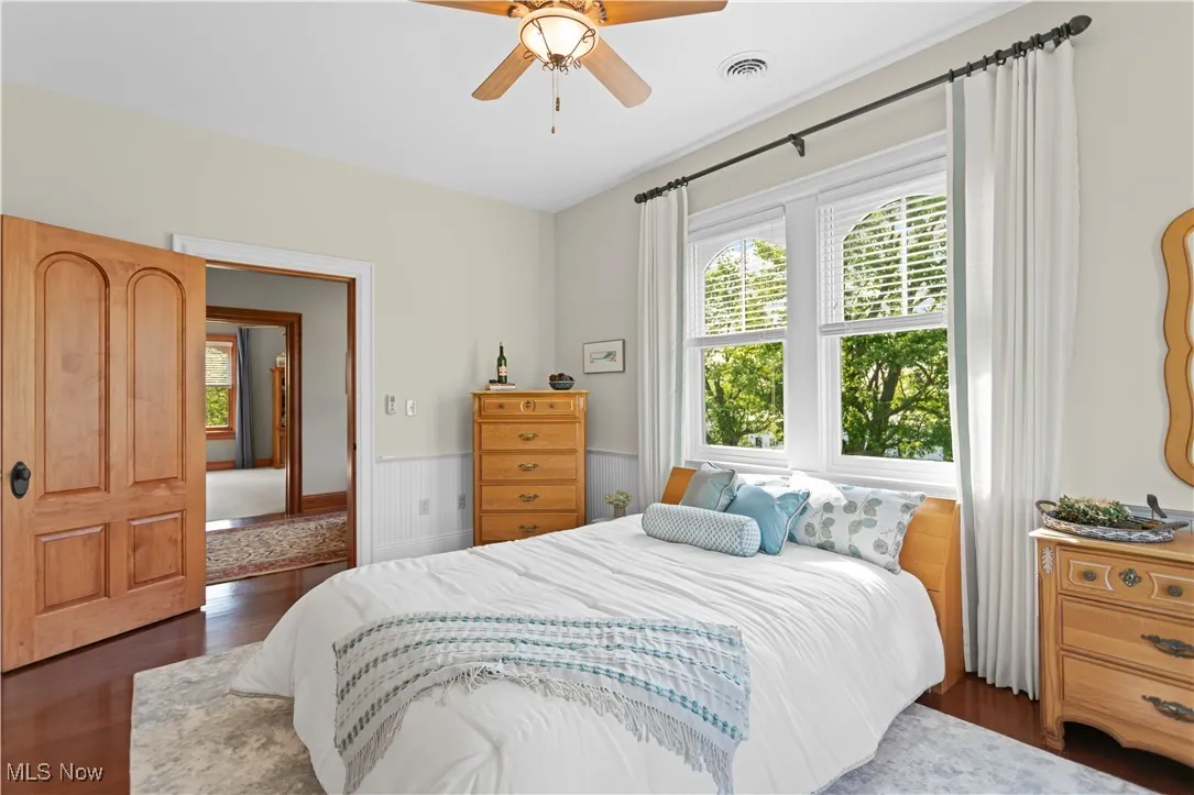 Bedroom with wood finished floors, a wainscoted wall, and ceiling fan