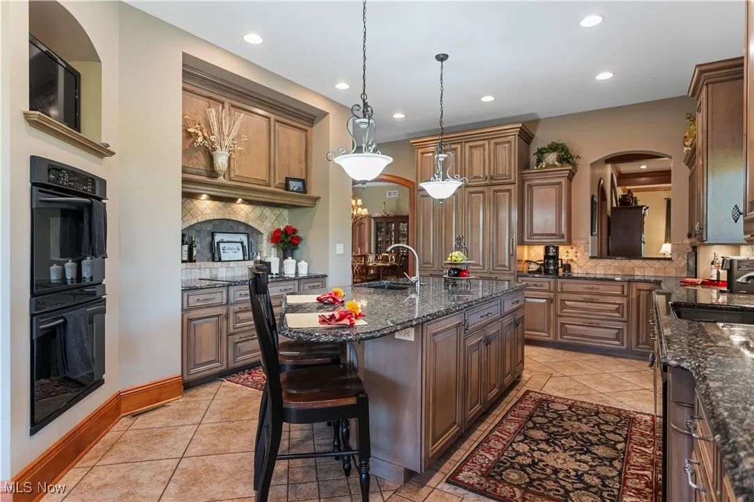Kitchen featuring decorative backsplash, recessed lighting, a sink, pendant lighting, and dark stone countertops