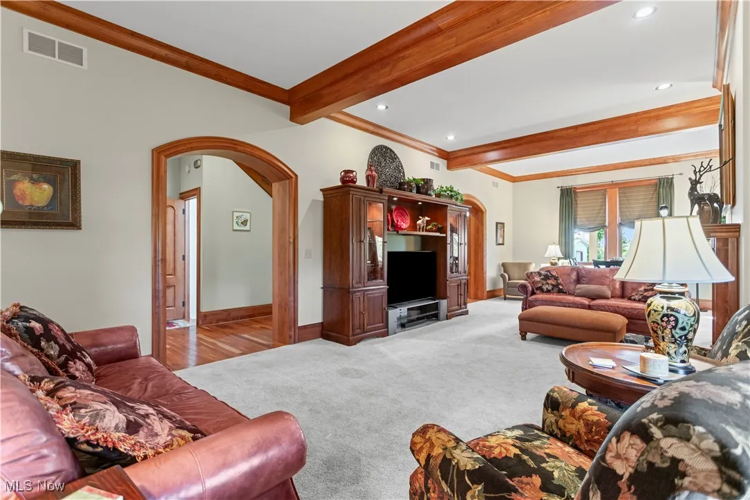 Carpeted living room with arched walkways, ornamental molding, beamed ceiling, recessed lighting, and baseboards