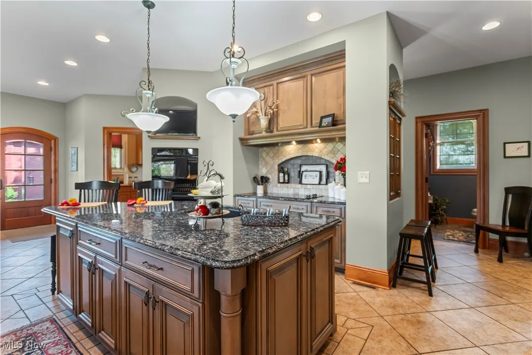 Kitchen featuring backsplash, recessed lighting, a center island, decorative light fixtures, and dark stone countertops