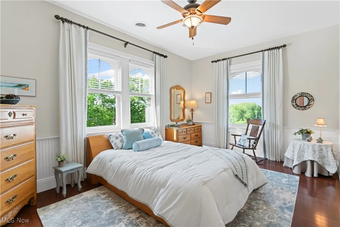Bedroom featuring a wainscoted wall, multiple windows, wood finished floors, and ceiling fan