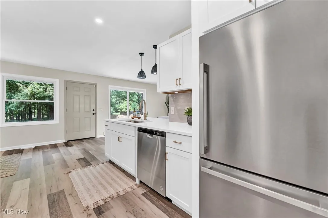 Kitchen with stainless steel appliances, a sink, light countertops, white cabinetry, and light wood-style flooring