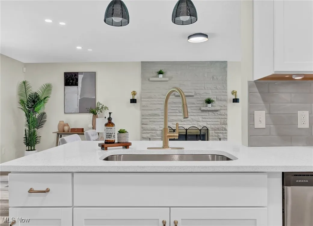 Kitchen featuring a sink, dishwasher, white cabinetry, tasteful backsplash, and light stone countertops