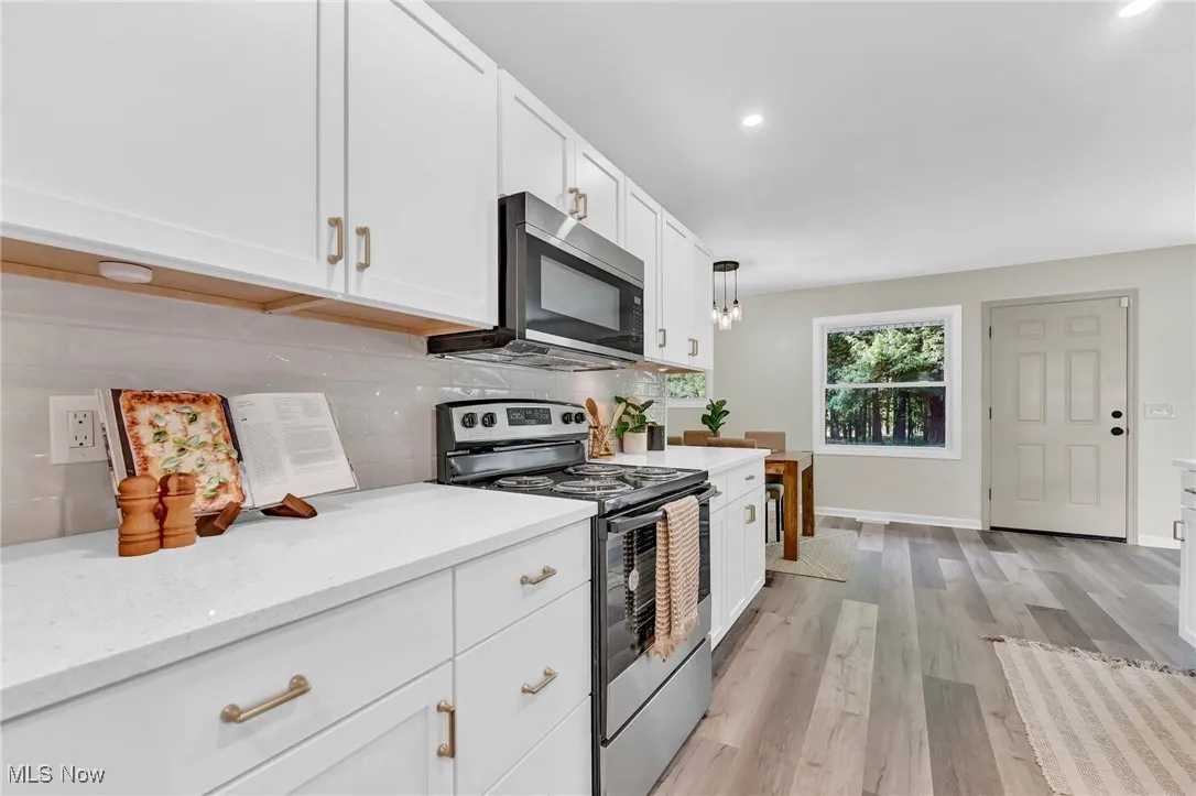 Kitchen featuring stainless steel appliances, tasteful backsplash, white cabinetry, light wood-style floors, and light stone counters