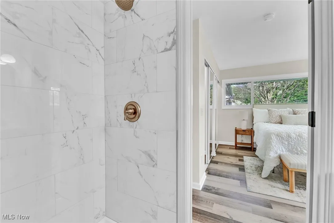 Ensuite bathroom featuring tiled shower, wood finished floors, and baseboards