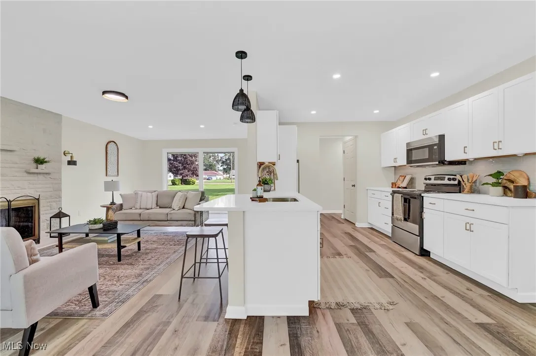 Kitchen featuring stainless steel appliances, a sink, open floor plan, light wood-style flooring, and light countertops