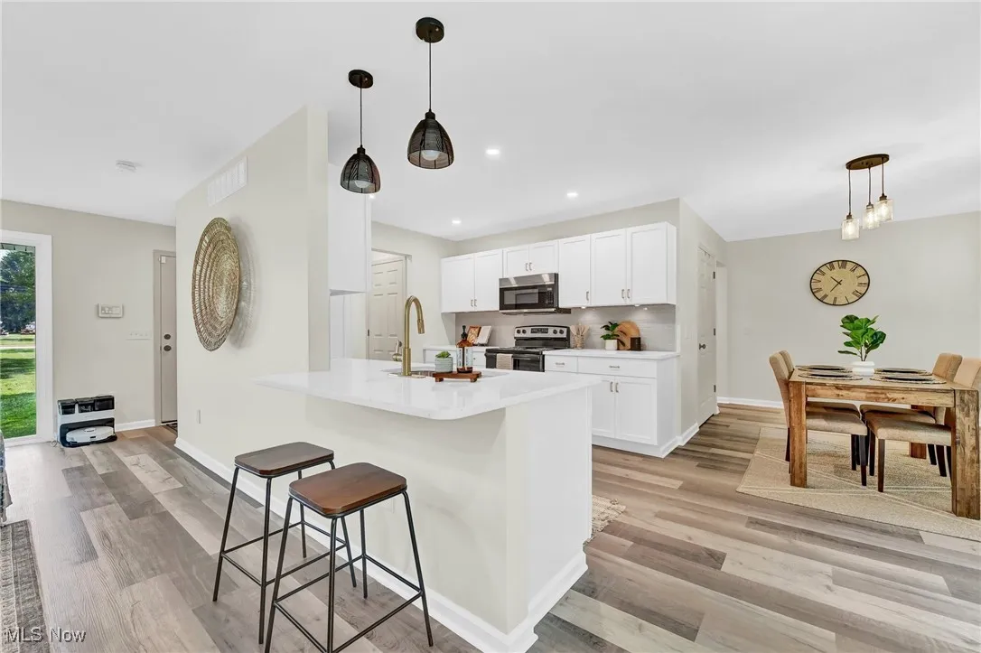 Kitchen featuring stainless steel appliances, a kitchen breakfast bar, light wood-type flooring, a sink, and white cabinets