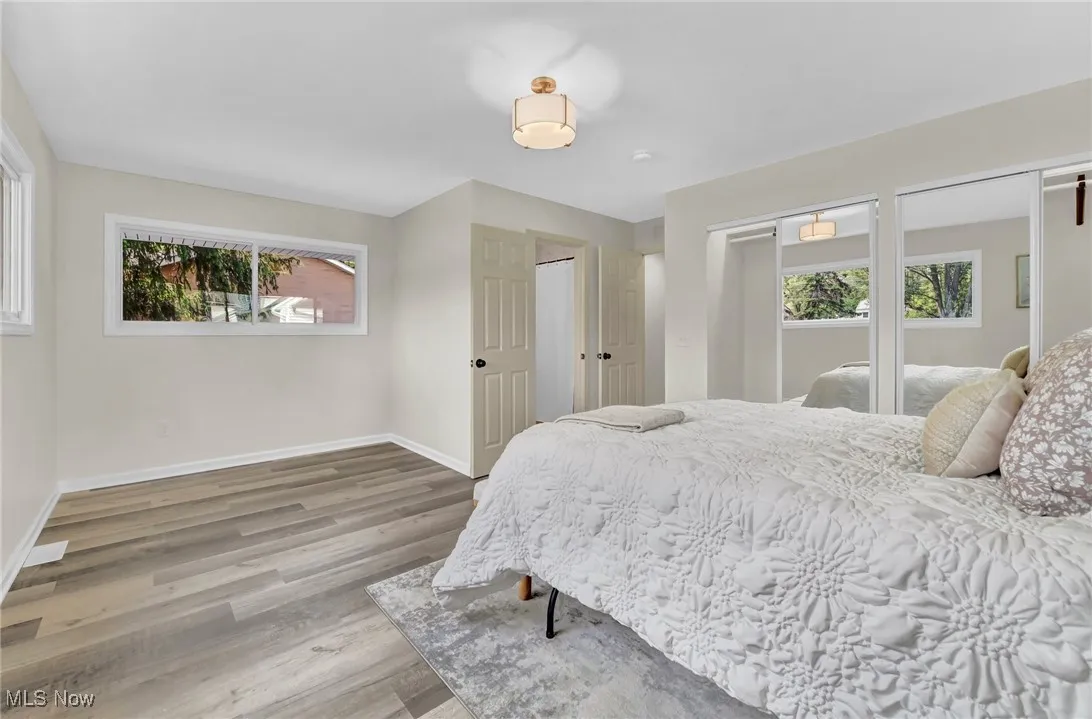 Bedroom with multiple windows, baseboards, wood finished floors, and two closets