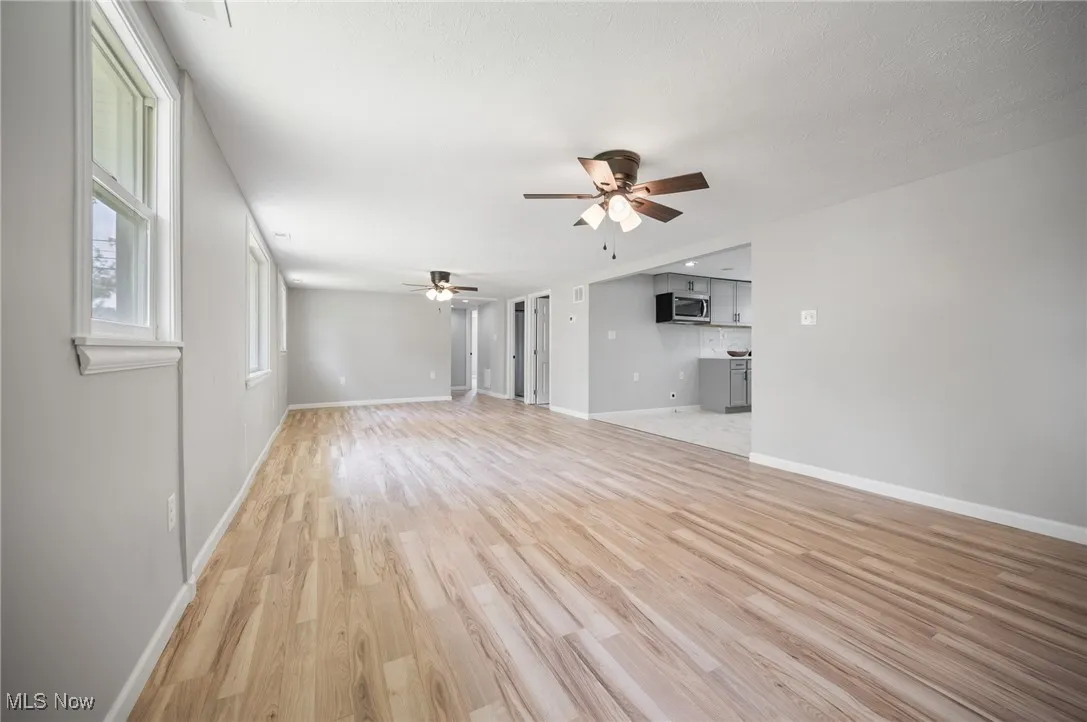 Unfurnished living room featuring a ceiling fan, light wood-style floors, and baseboards