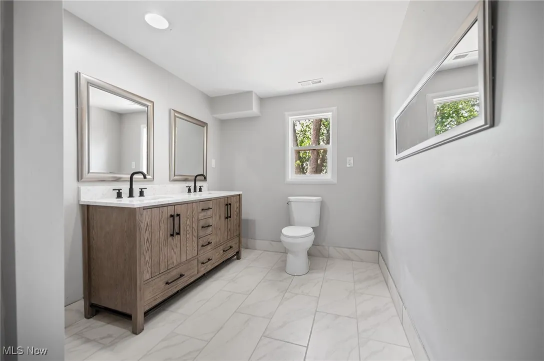 Full bathroom featuring marble look tile flooring, double vanity, toilet, and baseboards