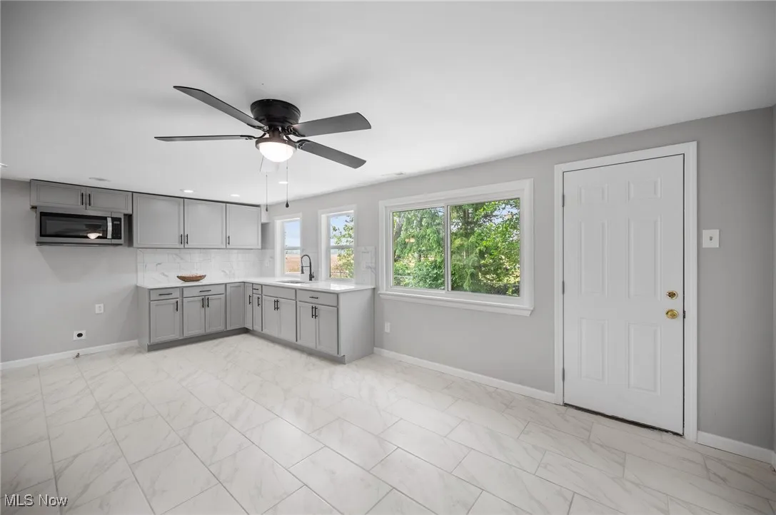 Kitchen featuring gray cabinets, stainless steel microwave, a sink, and baseboards