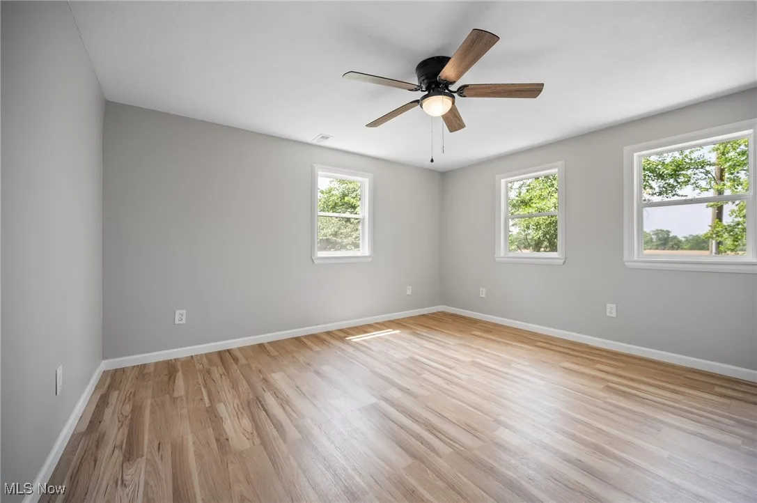 Unfurnished room featuring healthy amount of natural light, baseboards, light wood-type flooring, and ceiling fan