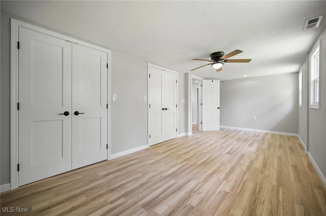 Unfurnished bedroom with light wood-type flooring, baseboards, a ceiling fan, a textured ceiling, and multiple closets