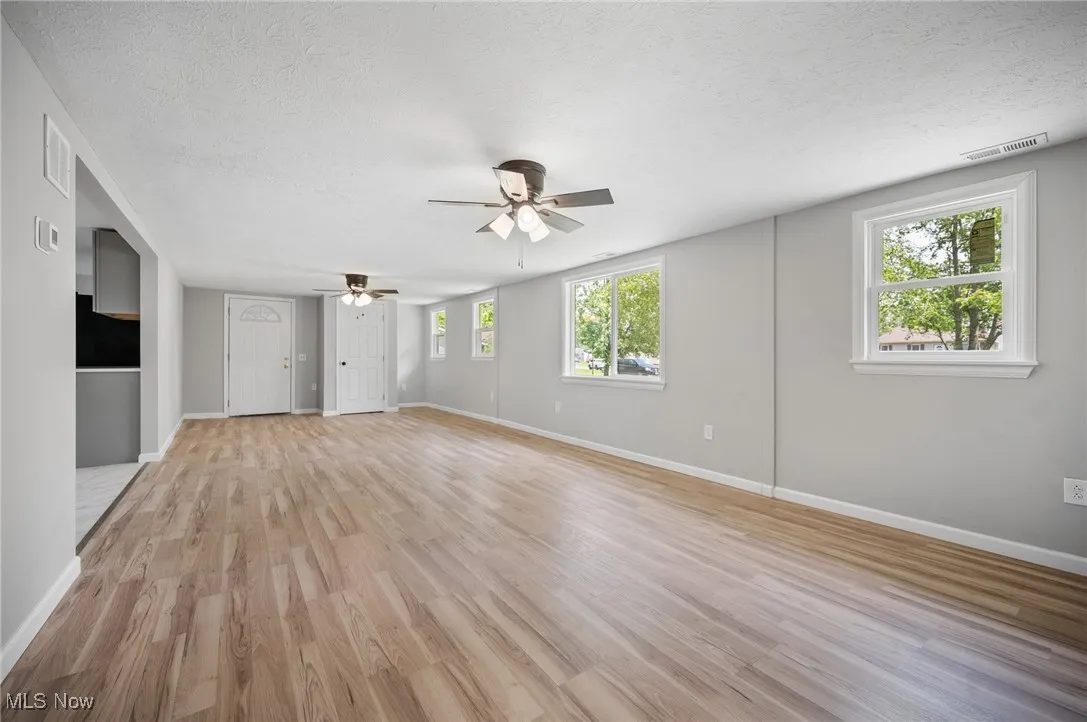 Unfurnished living room with a ceiling fan, light wood-style floors, a textured ceiling, and baseboards