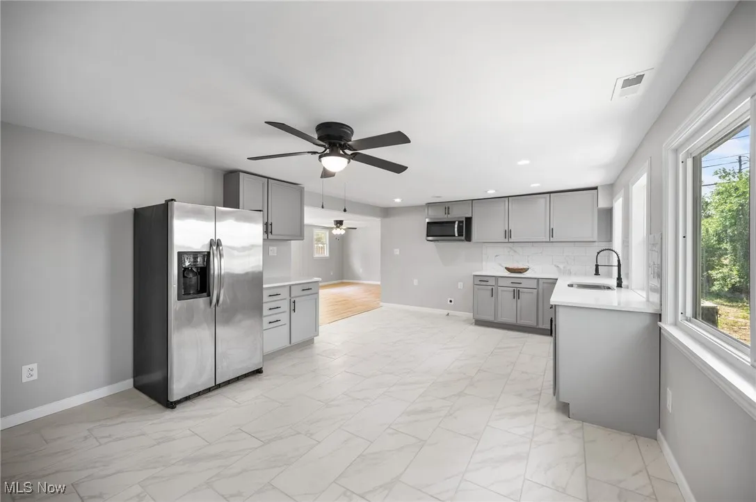 Kitchen with stainless steel appliances, gray cabinets, ceiling fan, light marble finish floors, and recessed lighting