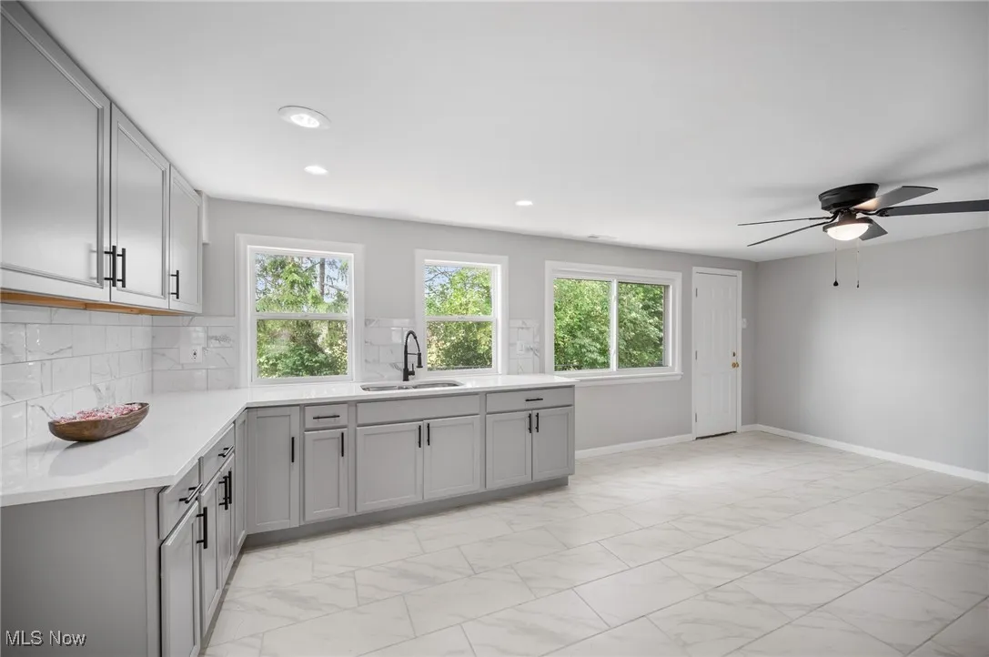 Kitchen featuring a sink, gray cabinetry, light countertops, light marble finish flooring, and a ceiling fan