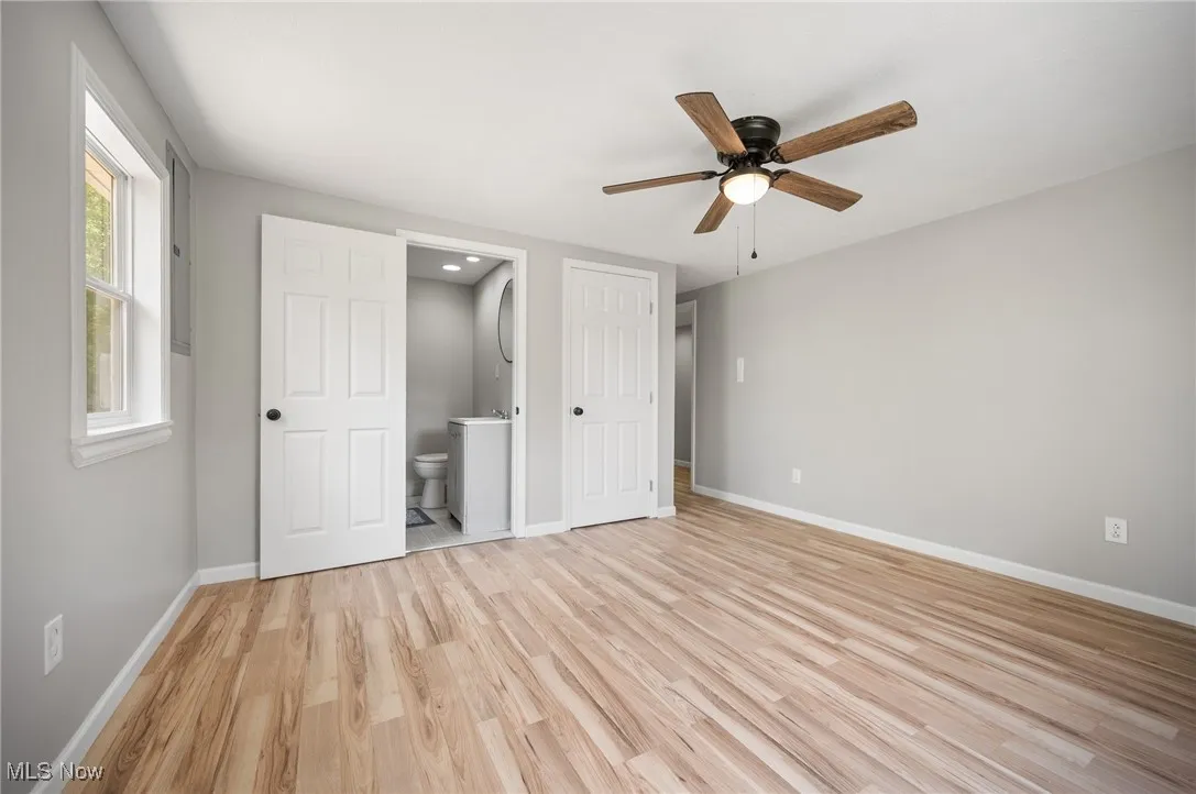 Unfurnished bedroom featuring light wood-style floors, baseboards, ensuite bath, and ceiling fan