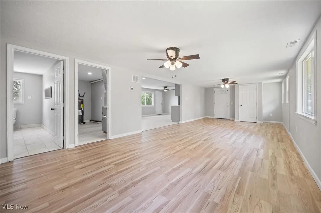 Unfurnished living room with ceiling fan, light wood finished floors, and baseboards
