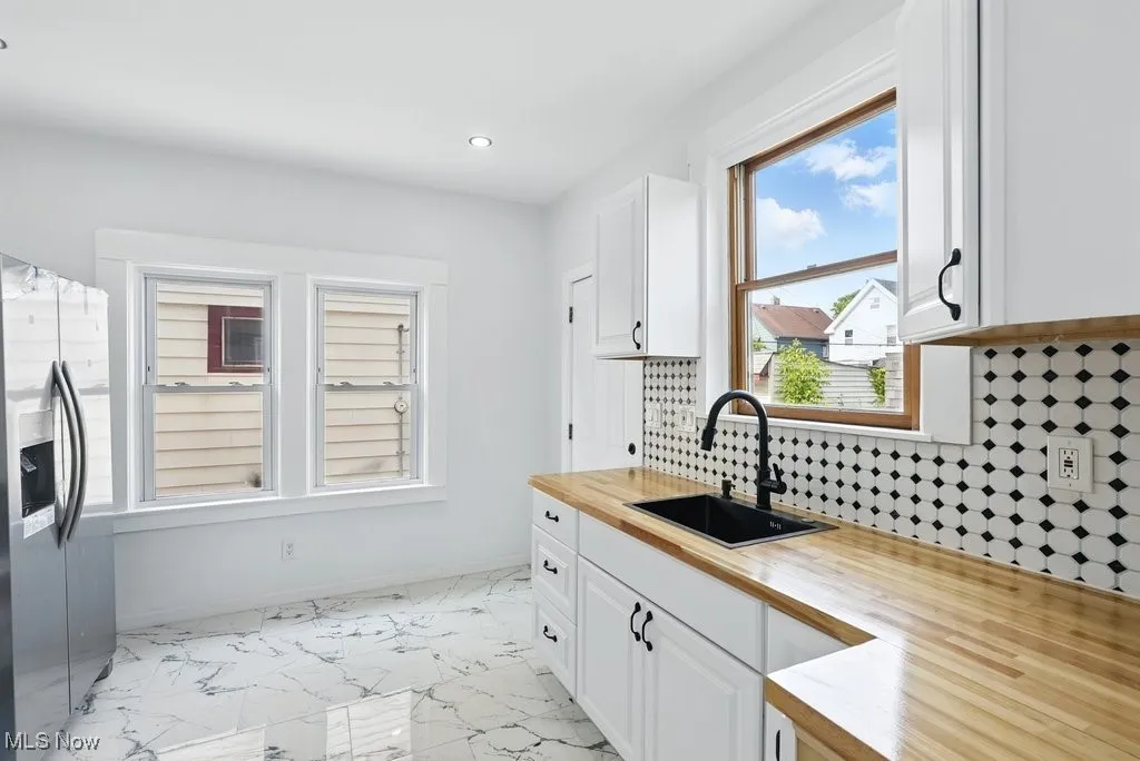 Kitchen featuring a sink, wood counters, stainless steel fridge, white cabinets, and recessed lighting