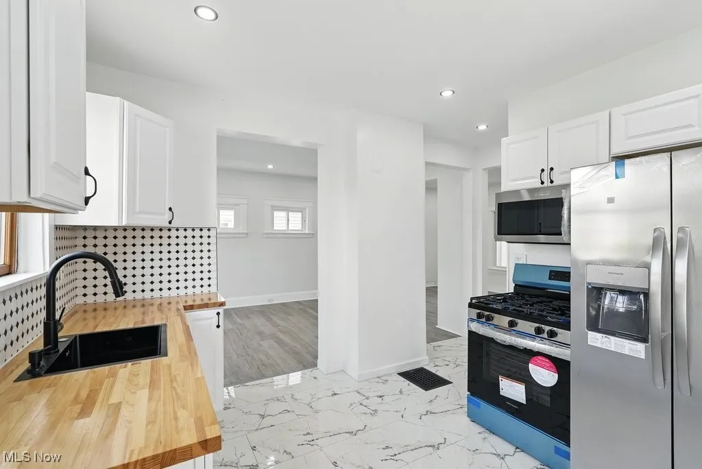 Kitchen with stainless steel appliances, a sink, wooden counters, white cabinetry, and recessed lighting