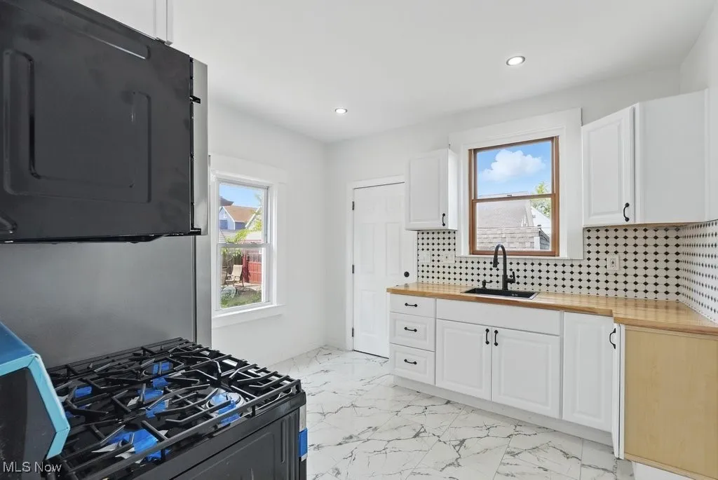 Kitchen with wooden counters, a sink, gas stove, light marble finish floors, and backsplash