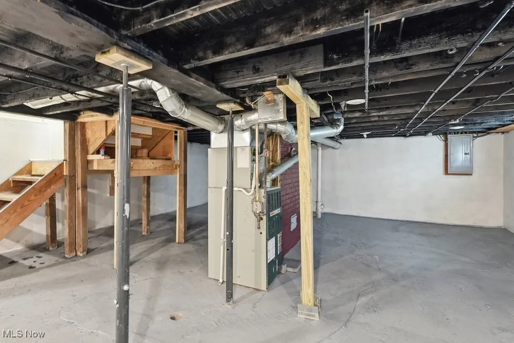 Unfinished below grade area featuring electric panel, stairway, and heating unit