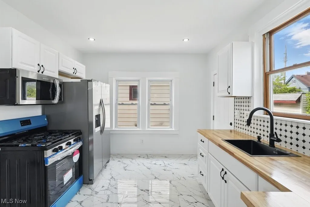 Kitchen with stainless steel appliances, wood counters, a sink, light marble finish floors, and plenty of natural light
