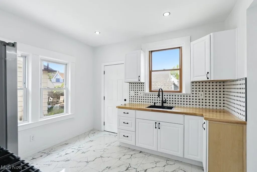 Kitchen featuring a sink, light marble finish flooring, recessed lighting, backsplash, and white cabinets