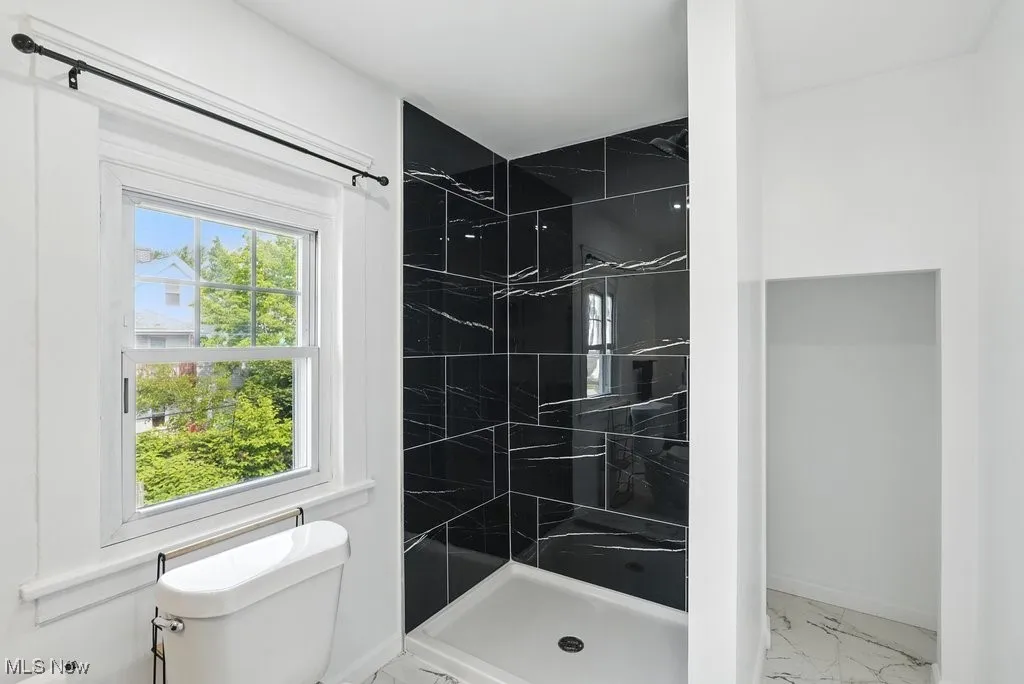 Bathroom with marble finish flooring, a stall shower, toilet, and baseboards