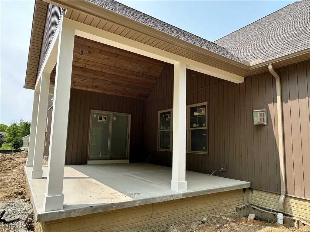 Entrance to property featuring a shingled roof and a patio