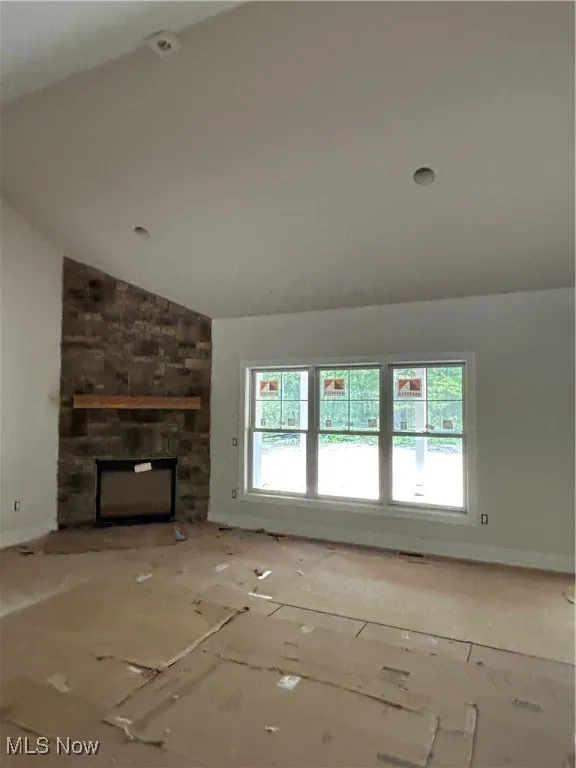 Unfurnished living room with healthy amount of natural light, vaulted ceiling, and a stone fireplace