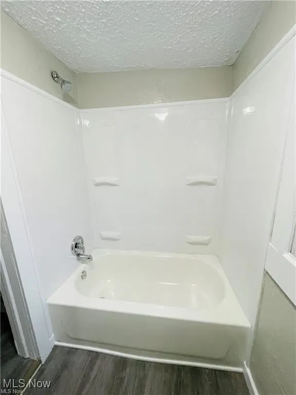 Bathroom featuring wood finished floors, a textured ceiling, and shower / washtub combination