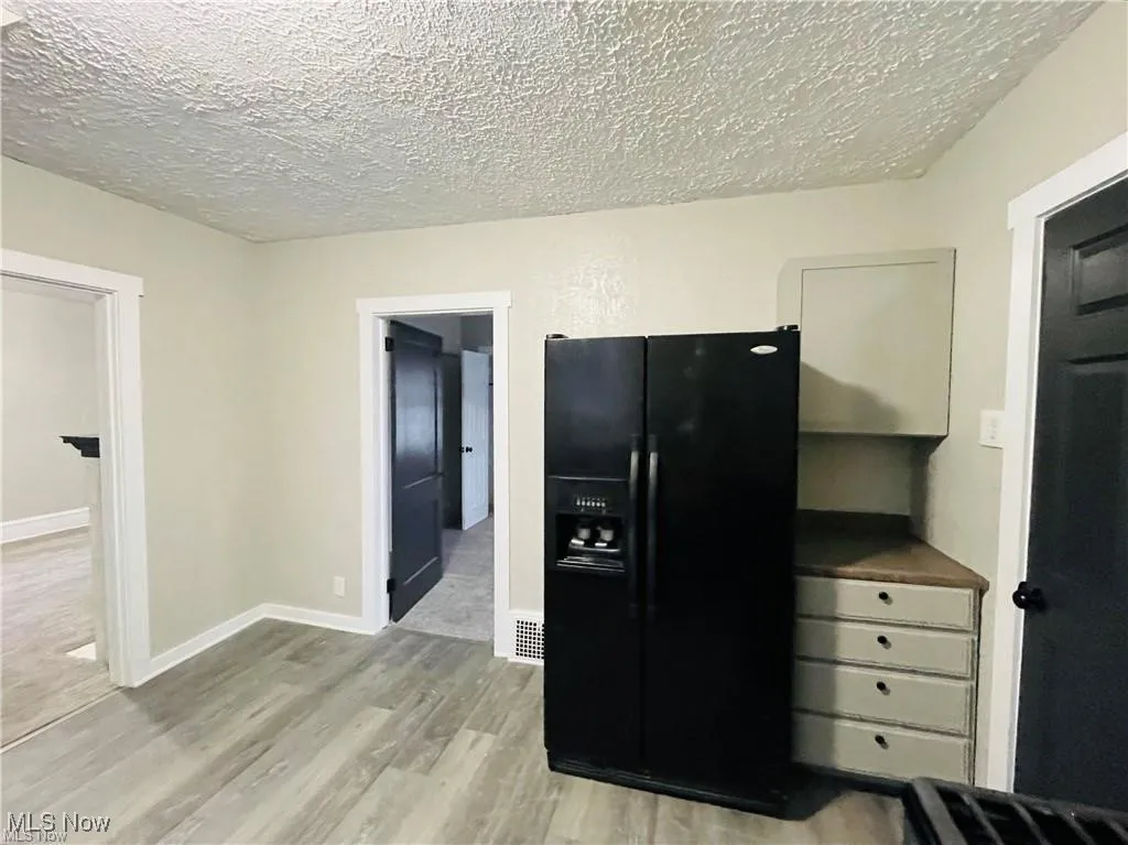 Kitchen with black fridge, a textured ceiling, wood finished floors, and baseboards