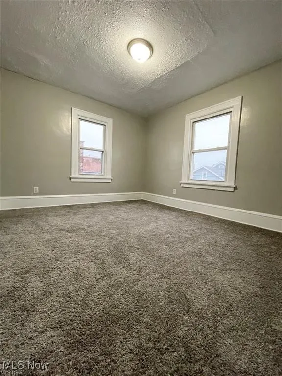 Spare room with a textured ceiling, carpet floors, and baseboards