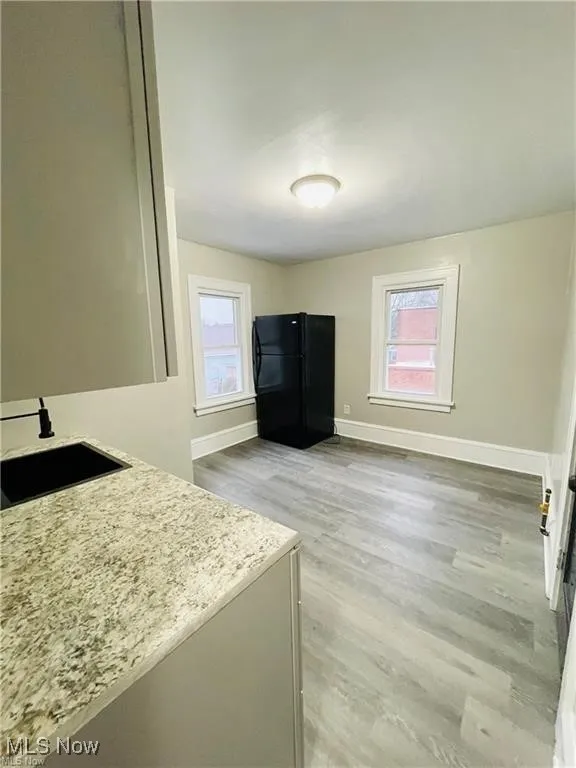 Kitchen featuring freestanding refrigerator, a sink, baseboards, light wood-style floors, and light stone countertops