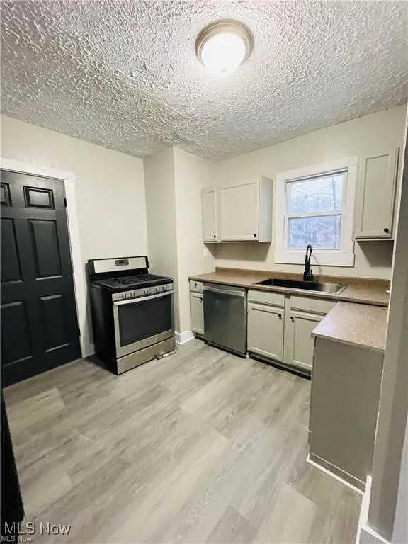 Kitchen featuring appliances with stainless steel finishes, a sink, a textured ceiling, light wood-type flooring, and white cabinets