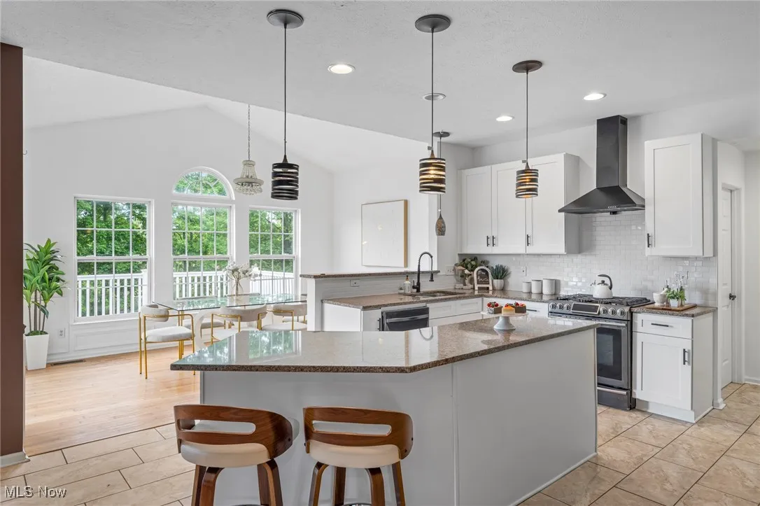 Kitchen featuring wall chimney exhaust hood, appliances with stainless steel finishes, a sink, vaulted ceiling, and a peninsula