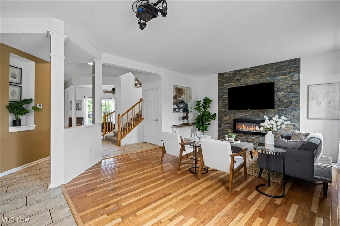 Living area with a stone fireplace, stairs, decorative columns, light wood-style floors, and baseboards