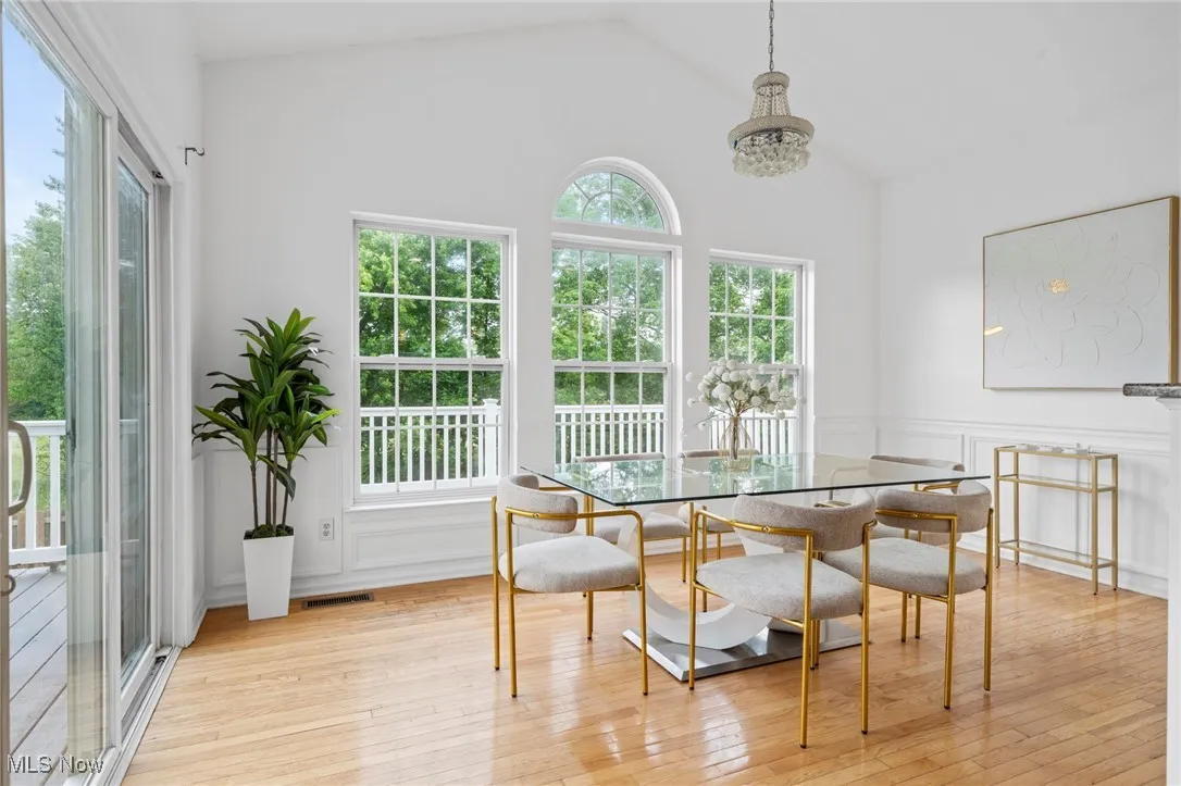 Dining room with breakfast area, light wood-style floors, high vaulted ceiling, a chandelier, and a decorative wall
