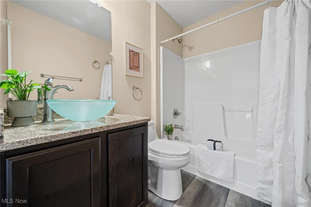 Bathroom with vanity, shower / bath combo, wood finished floors, and toilet