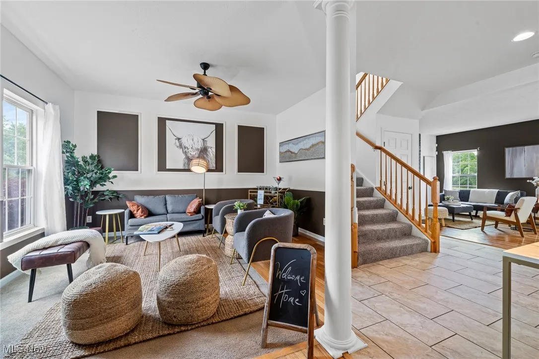 Living area featuring ornate columns, stairway, and ceiling fan