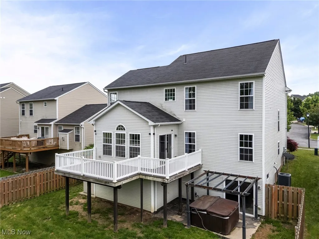 Back of property featuring a hot tub, a wooden deck, cooling unit, and roof with shingles