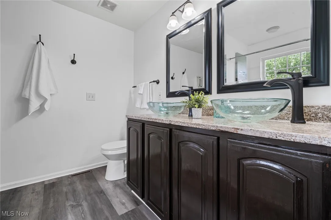 Bathroom featuring toilet, double vanity, wood finished floors, and baseboards