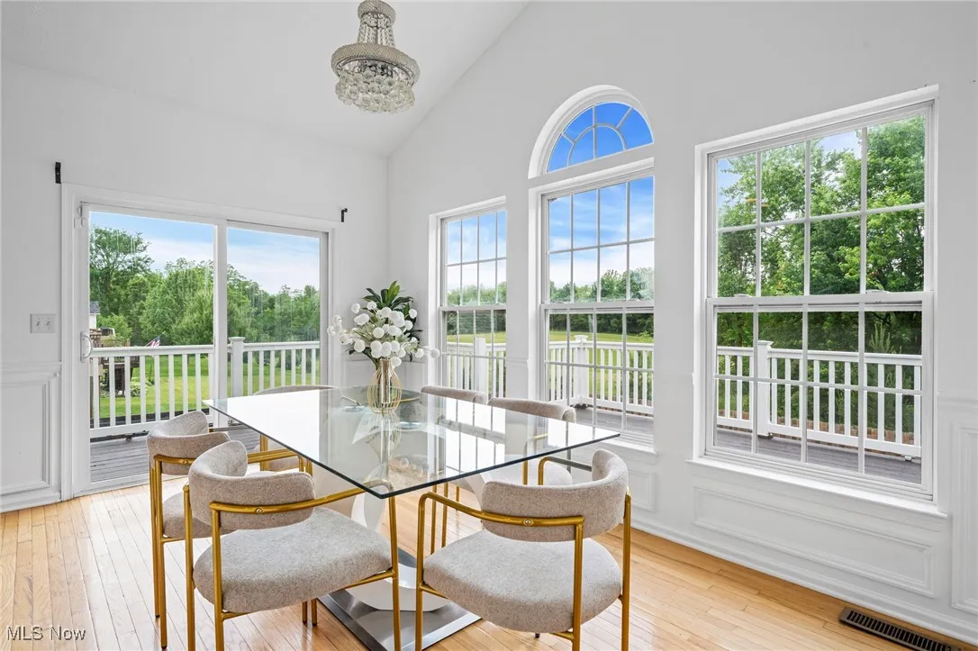 Dining space with healthy amount of natural light, light wood-type flooring, a chandelier, and high vaulted ceiling