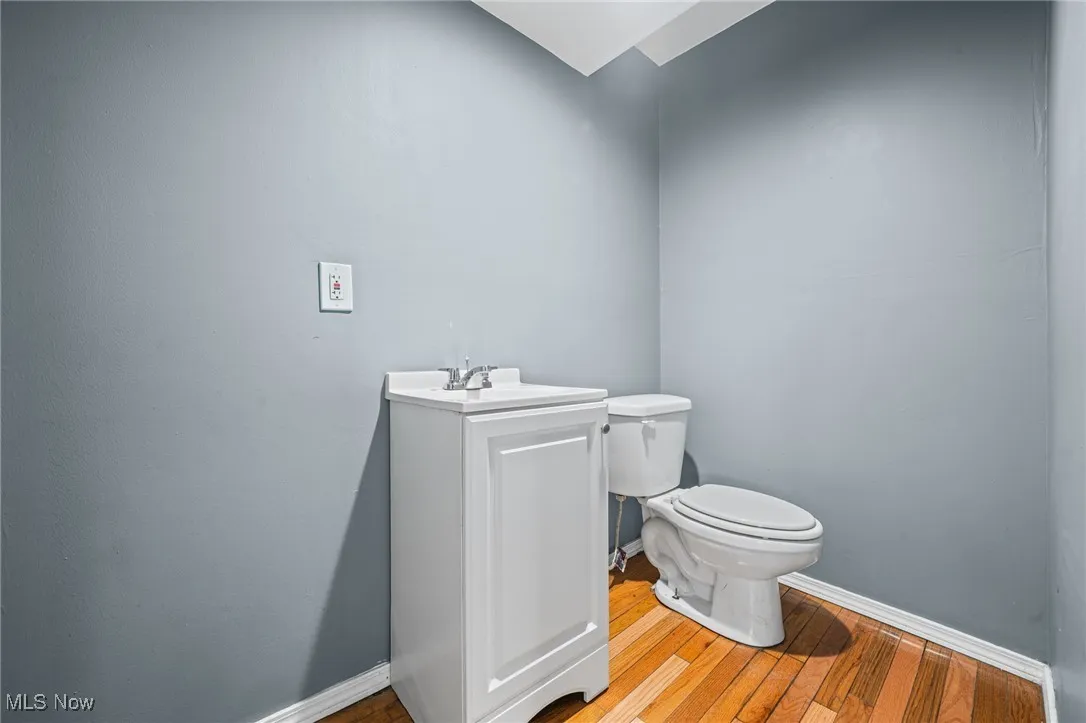 Half bathroom with toilet, wood finished floors, vanity, and baseboards