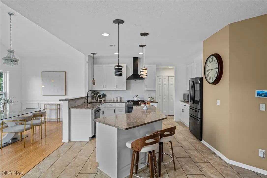 Kitchen with wall chimney range hood, appliances with stainless steel finishes, a sink, a kitchen island, and dark stone counters
