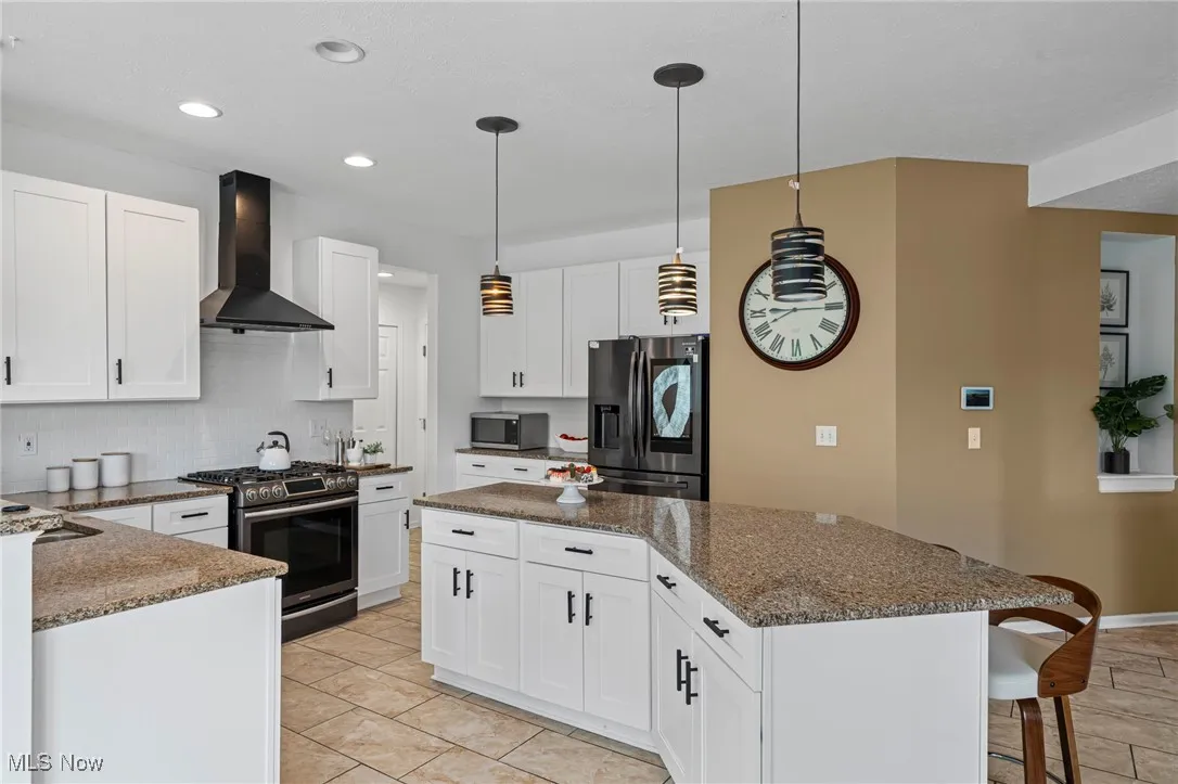 Kitchen with stainless steel appliances, wall chimney exhaust hood, a kitchen island, a breakfast bar area, and decorative backsplash