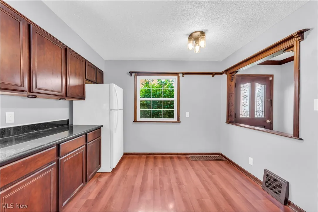 Kitchen with freestanding refrigerator, light wood-type flooring, a textured ceiling, baseboards, and dark stone countertops
