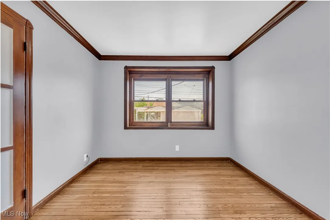 Empty room featuring light wood-style floors, crown molding, and baseboards